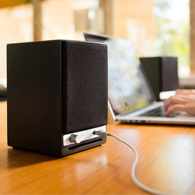 Audioengine A2-HD with headphones on a workspace.